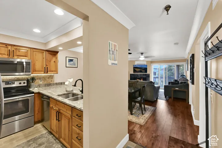 Kitchen featuring wood cabinetry, stone countertops, stainless steel appliances, and recessed lighting; living area with wood-finish flooring and a fireplace