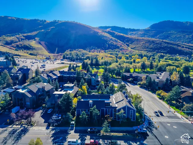 Aerial perspective featuring multi-story residential structures with pitched rooflines, mature evergreen trees, and immediate access to regional thoroughfares, framed by a prominent mountain landscape