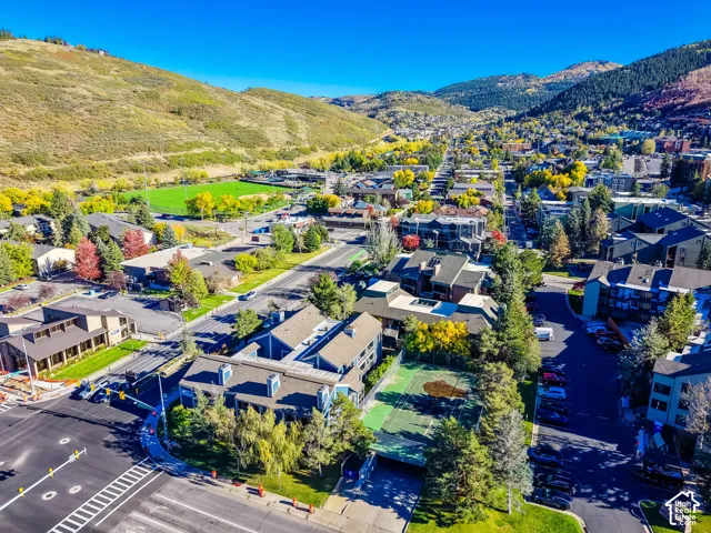 Aerial perspective of residential structures featuring a private hard-surface tennis court, shingle roofing, and mountain range backdrop