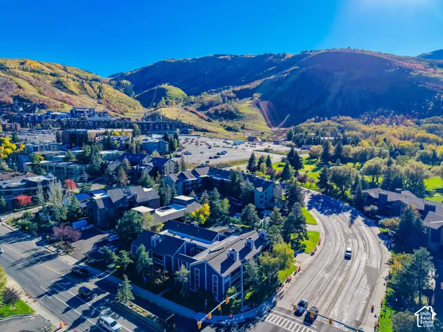Aerial perspective of multi-story buildings with pitched roofs, surrounded by mature trees, paved roadways, and mountainous terrain