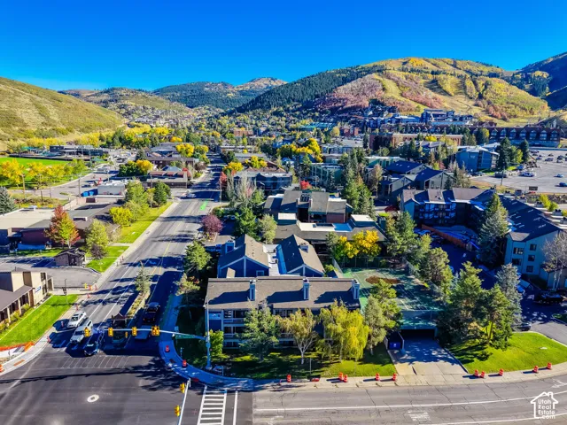 Aerial perspective of a multi-story residential complex featuring multiple chimneys, a paved driveway, and an on-site tennis court, set against a mountainous backdrop