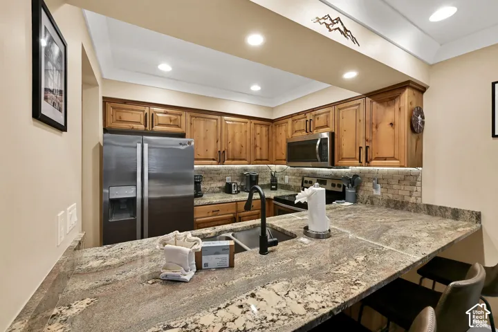Kitchen featuring natural-finish wood cabinetry, stone countertops, stone tile backsplash, stainless steel appliances, and matte black faucet fixtures