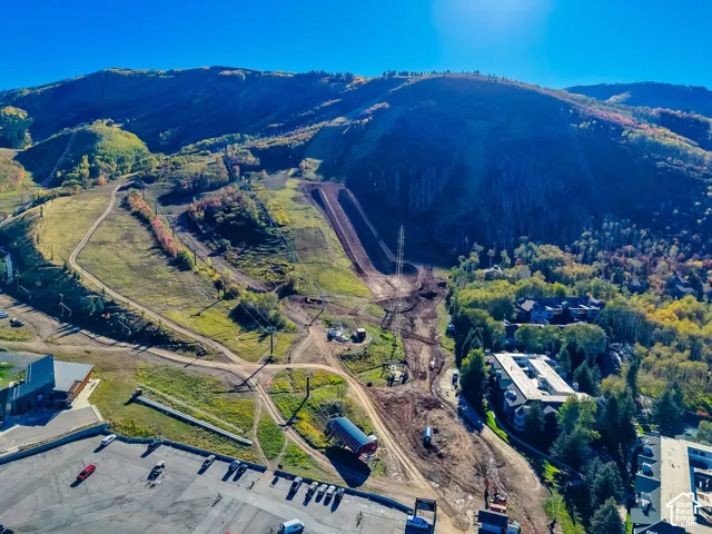 Aerial perspective featuring mountainous terrain with ski lift infrastructure, paved parking surfaces, and dense evergreen foliage