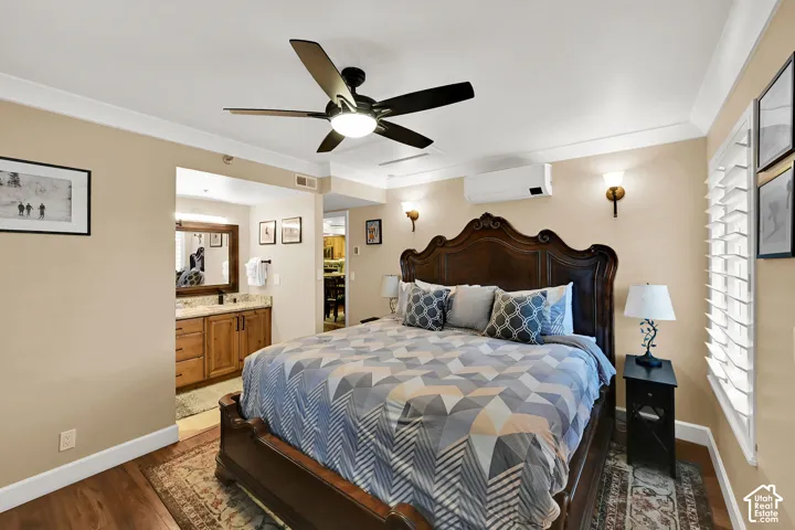 Wood-finish flooring, ceiling fan with integrated lighting, wall-mounted ductless climate control unit, plantation shutters, and wood vanity cabinetry with stone surfacing