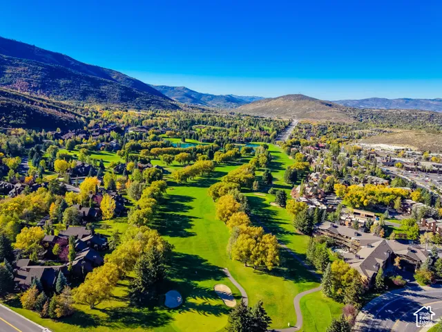 Aerial perspective of a golf course featuring manicured fairways, sand bunkers, mature deciduous trees, and mountain terrain in the distance