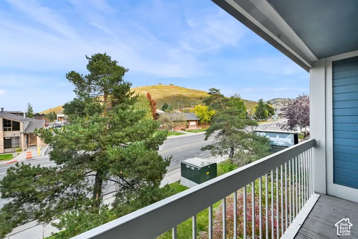 Private balcony with metal railing, blue horizontal siding, and wood-finish decking featuring a prominent mountain backdrop