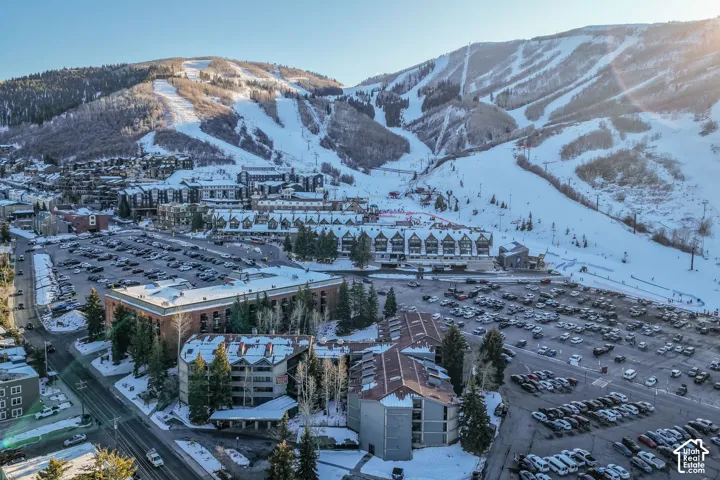 Aerial perspective featuring snow-covered mountain terrain, evergreen forest, and multi-story structural architecture with pitched roofing