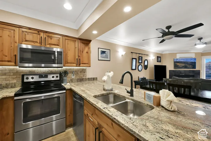 Kitchen featuring wood cabinetry, stone countertops, stainless steel appliances, brick-style tile backsplash, and a dual-basin undermount sink with a matte black faucet