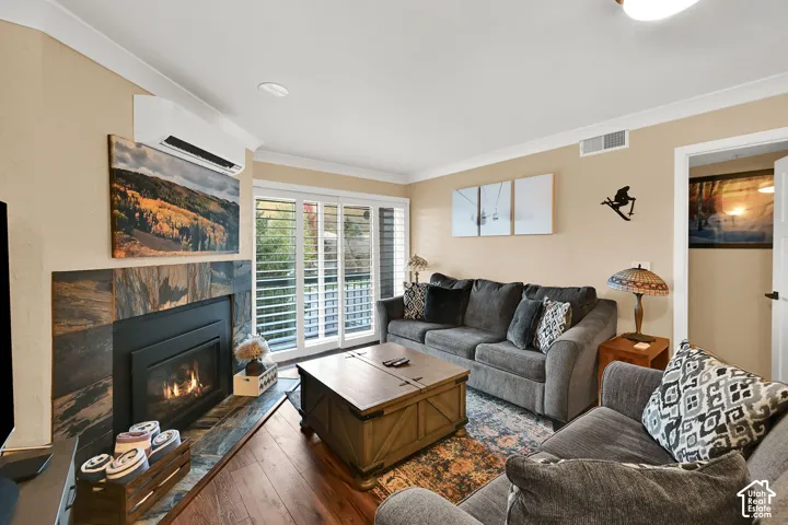 Fireplace with stone-finish surround, wood-finish flooring, wall-mounted heating and cooling unit, and sliding glass doors with shutter-style blinds