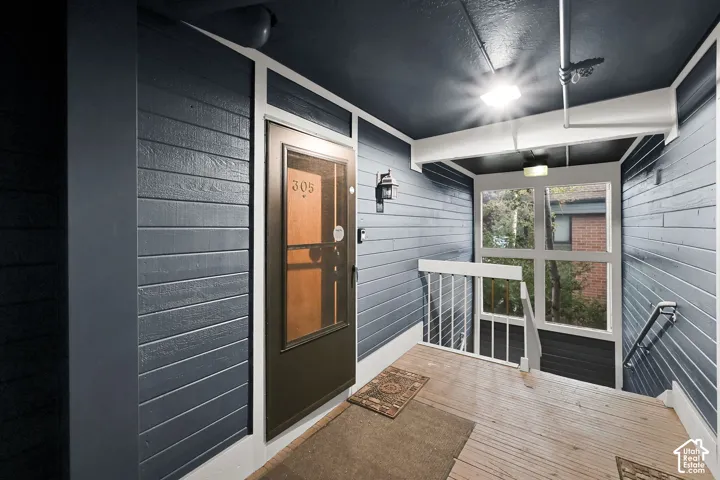 Exterior entry featuring dark blue horizontal siding, white trim accents, a wood-finish floor, and a full-light storm door