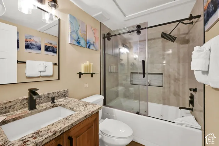 Bathroom featuring a stone-look countertop vanity, rectangular undermount sink, matte black faucet, and a jetted tub with a sliding glass enclosure and rainfall shower head