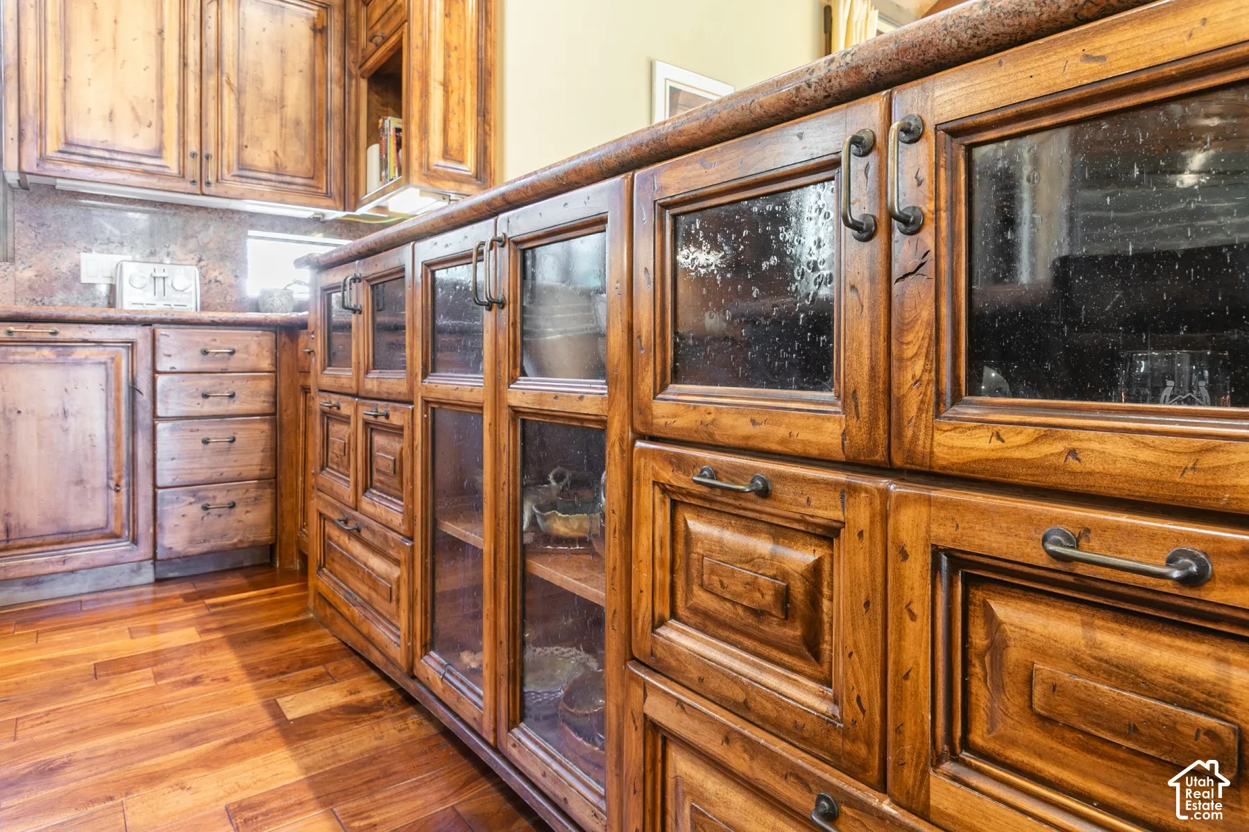 Custom stained-wood cabinetry featuring glass-paneled display doors, stone countertops, and dark metal hardware throughout