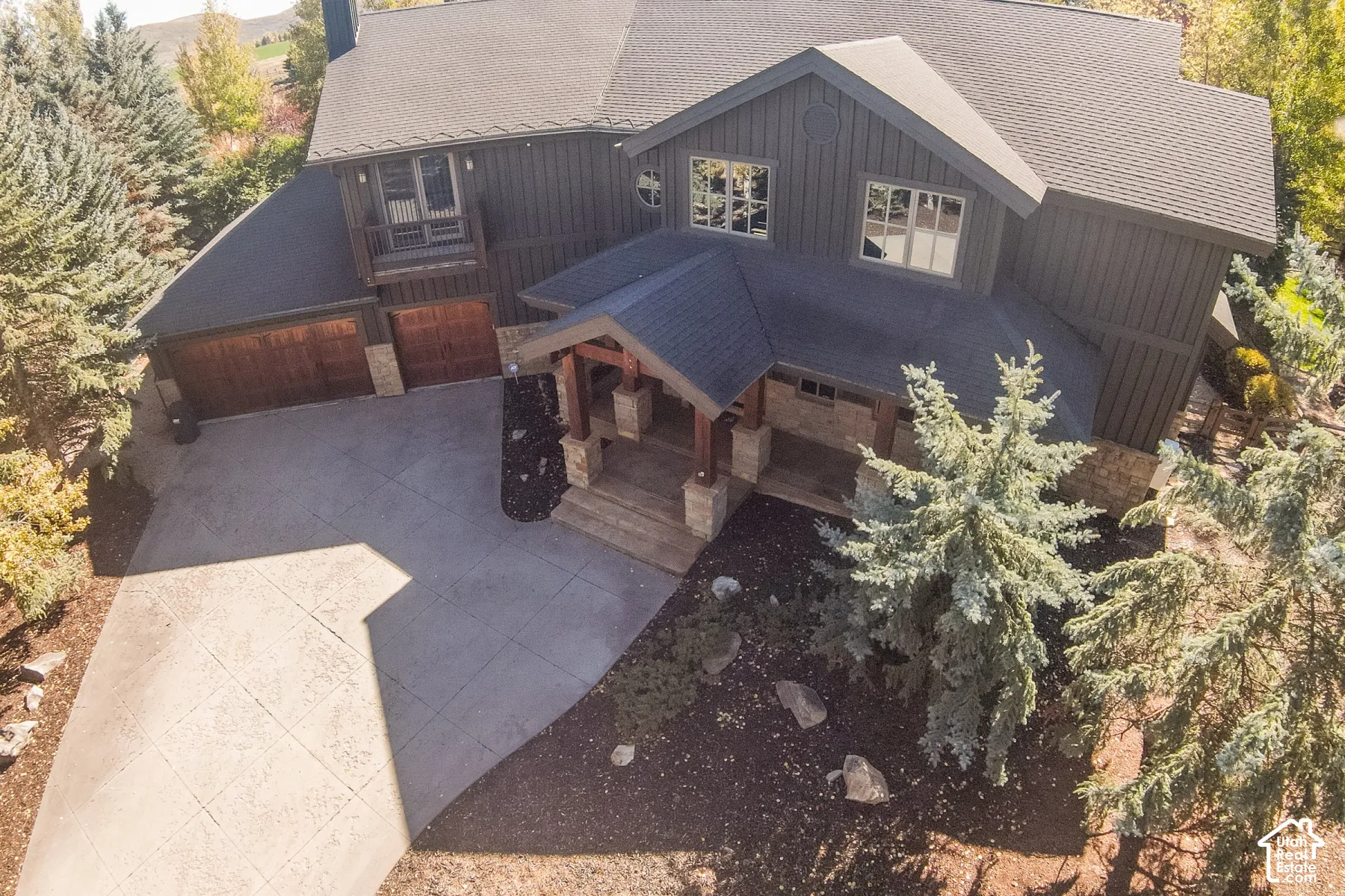 Multi-level exterior featuring dark vertical siding, stone masonry accents, a covered front entryway with timber posts, and a paved concrete driveway
