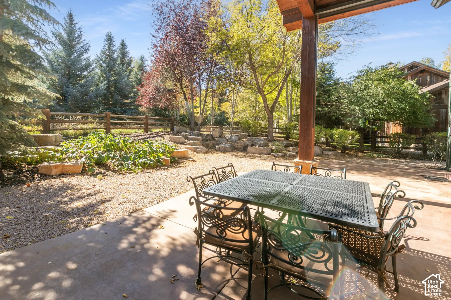 Covered concrete patio featuring timber post construction, gravel landscaping, tiered stone retaining walls, and split-rail wooden fencing