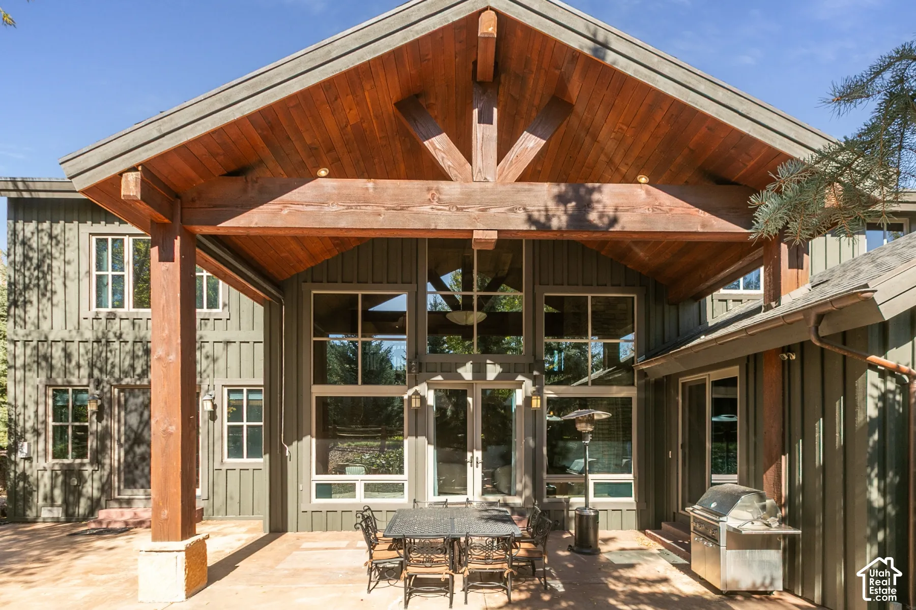 Covered patio featuring a timber-frame gable roof, vertical siding, floor-to-ceiling multi-pane windows, and a paved stone floor