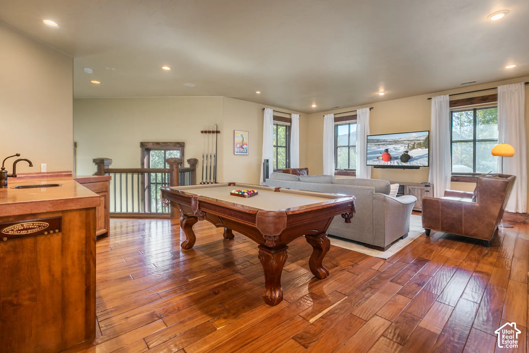 Wood-finish flooring, built-in wet bar with a copper-tone countertop, recessed lighting, and wooden staircase railing