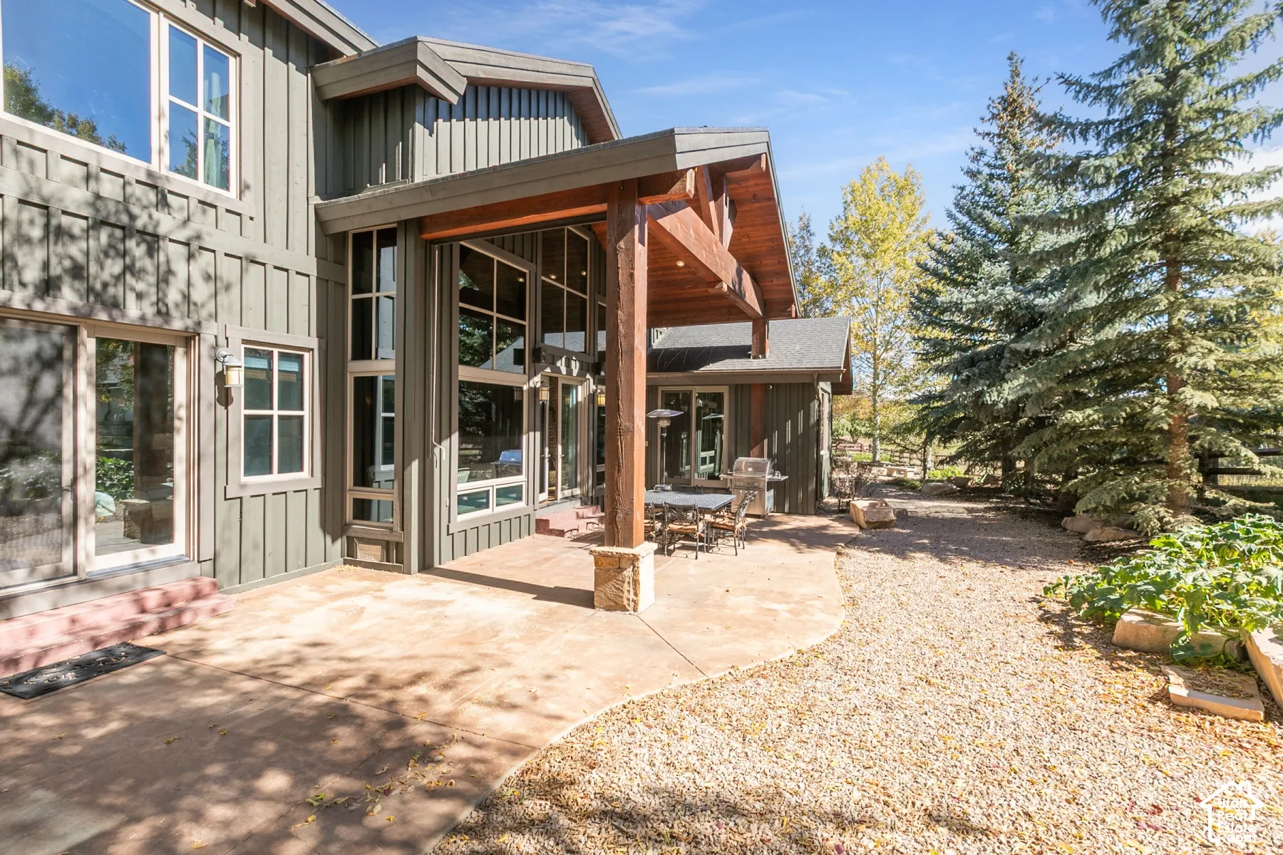 Exterior featuring board-and-batten siding, a covered patio with heavy timber supports, a concrete surface, and multi-story floor-to-ceiling windows