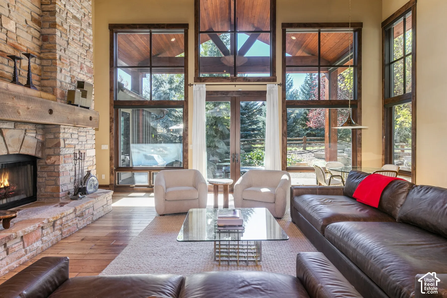 Floor-to-ceiling multi-pane windows, vaulted wood-plank ceiling, natural stone fireplace with timber mantel, and wood-finish flooring