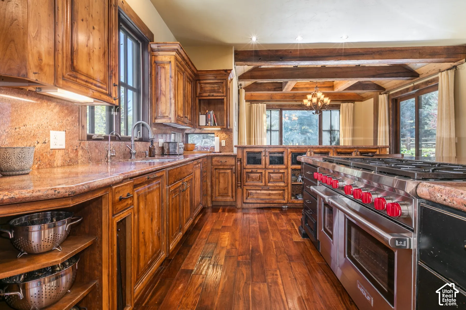 Kitchen featuring custom wood cabinetry, natural stone countertops, professional-grade stainless steel range, wood-finish flooring, and exposed ceiling beams