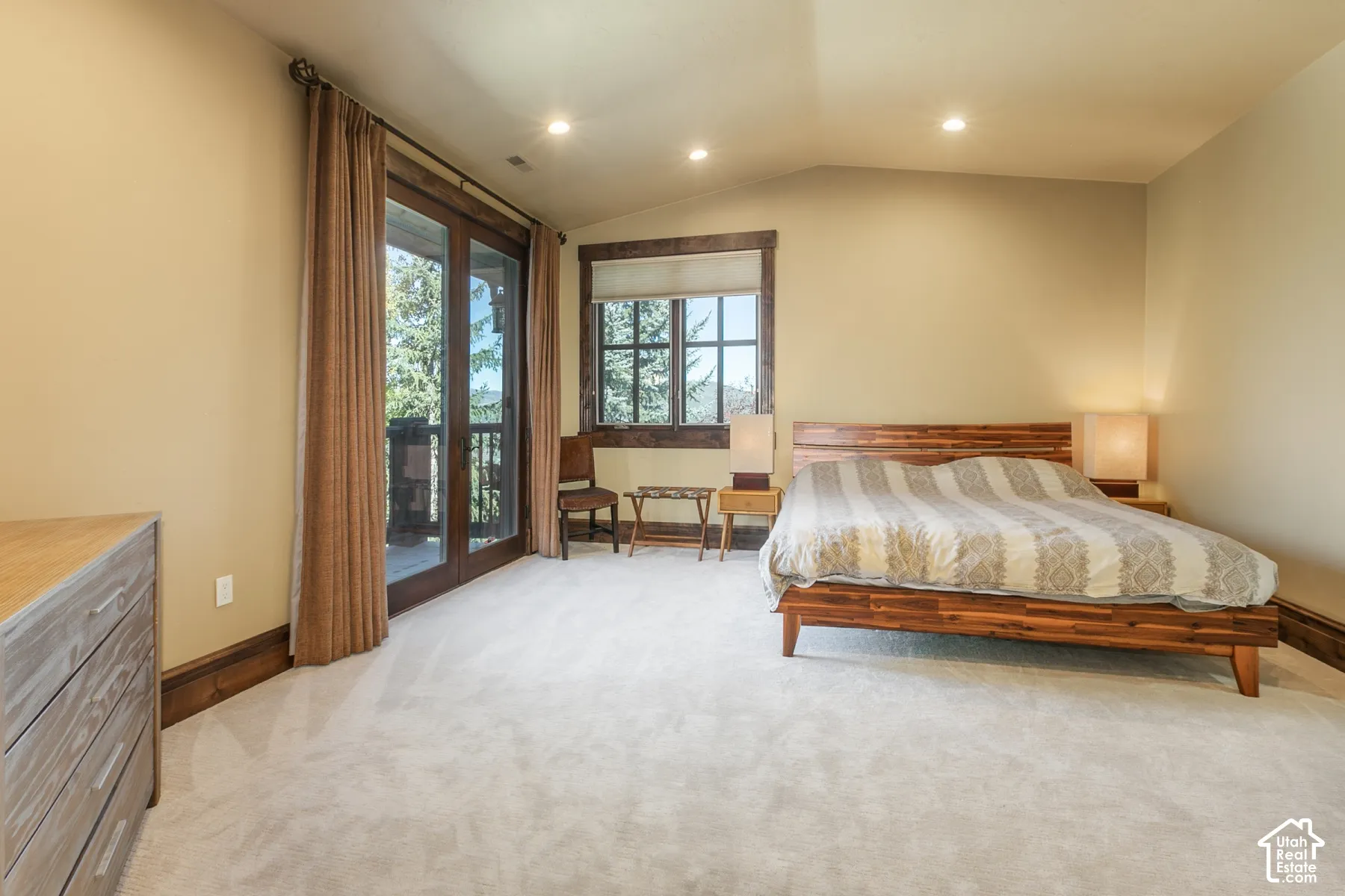 Vaulted ceilings featuring recessed lighting, carpeted flooring, and dark wood-trimmed window casings, including a glass-paned door opening to an exterior deck