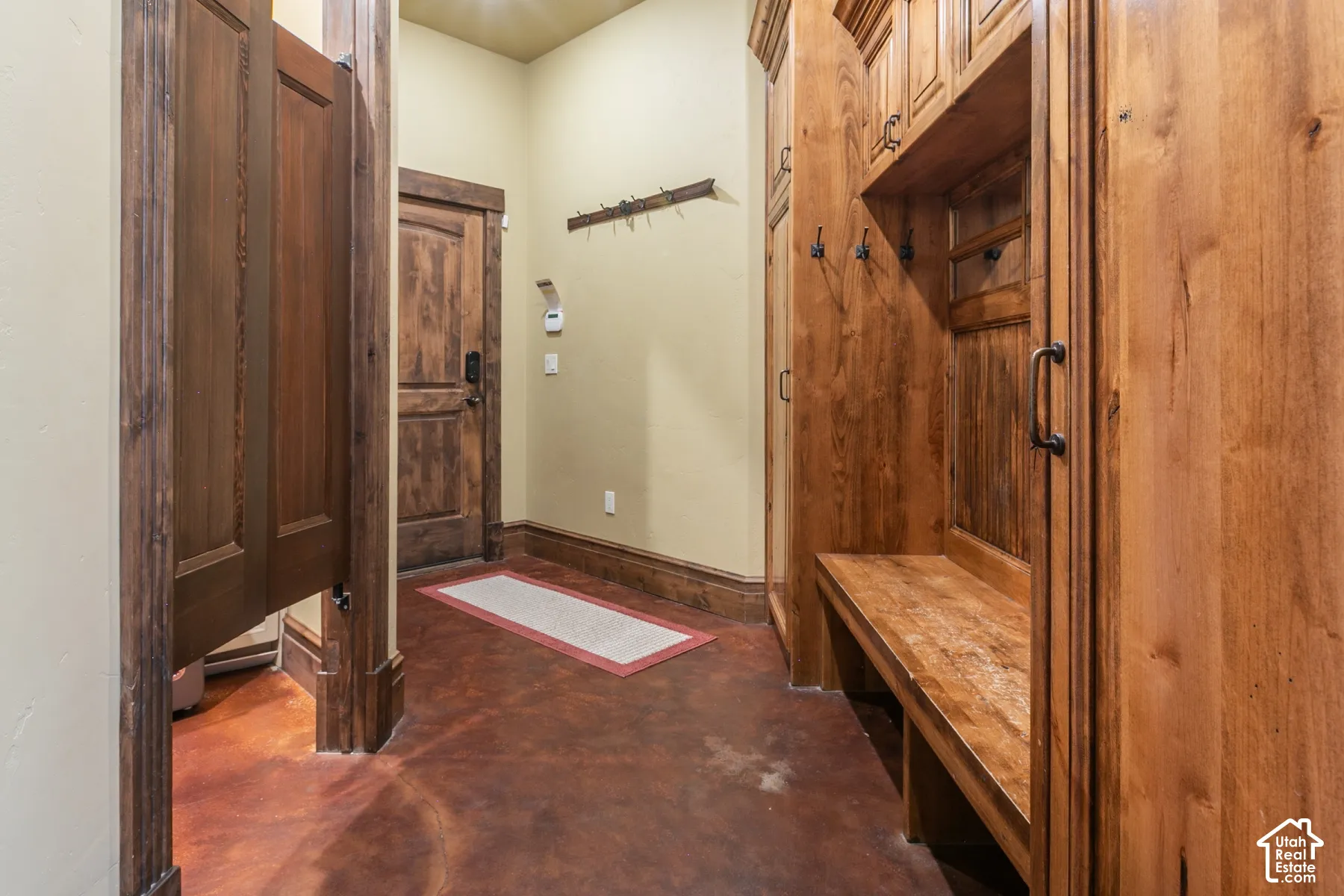 Mudroom featuring custom built-in wood cabinetry, integrated bench seating, dark-toned concrete flooring, and solid wood trim detailing