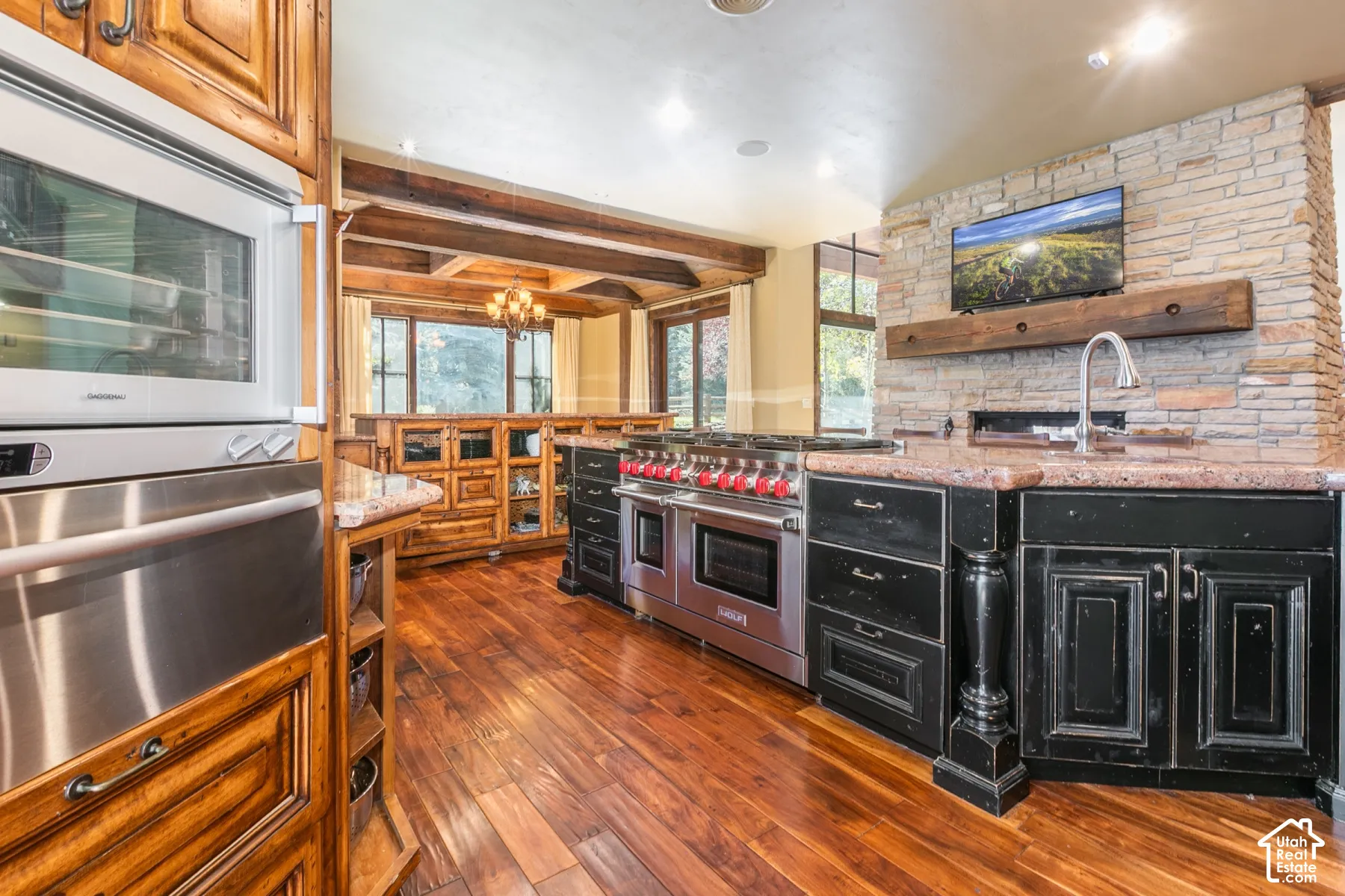 Kitchen featuring wood-finish flooring, exposed ceiling beams, custom cabinetry, a stacked-stone accent wall, and a stainless steel professional-grade range