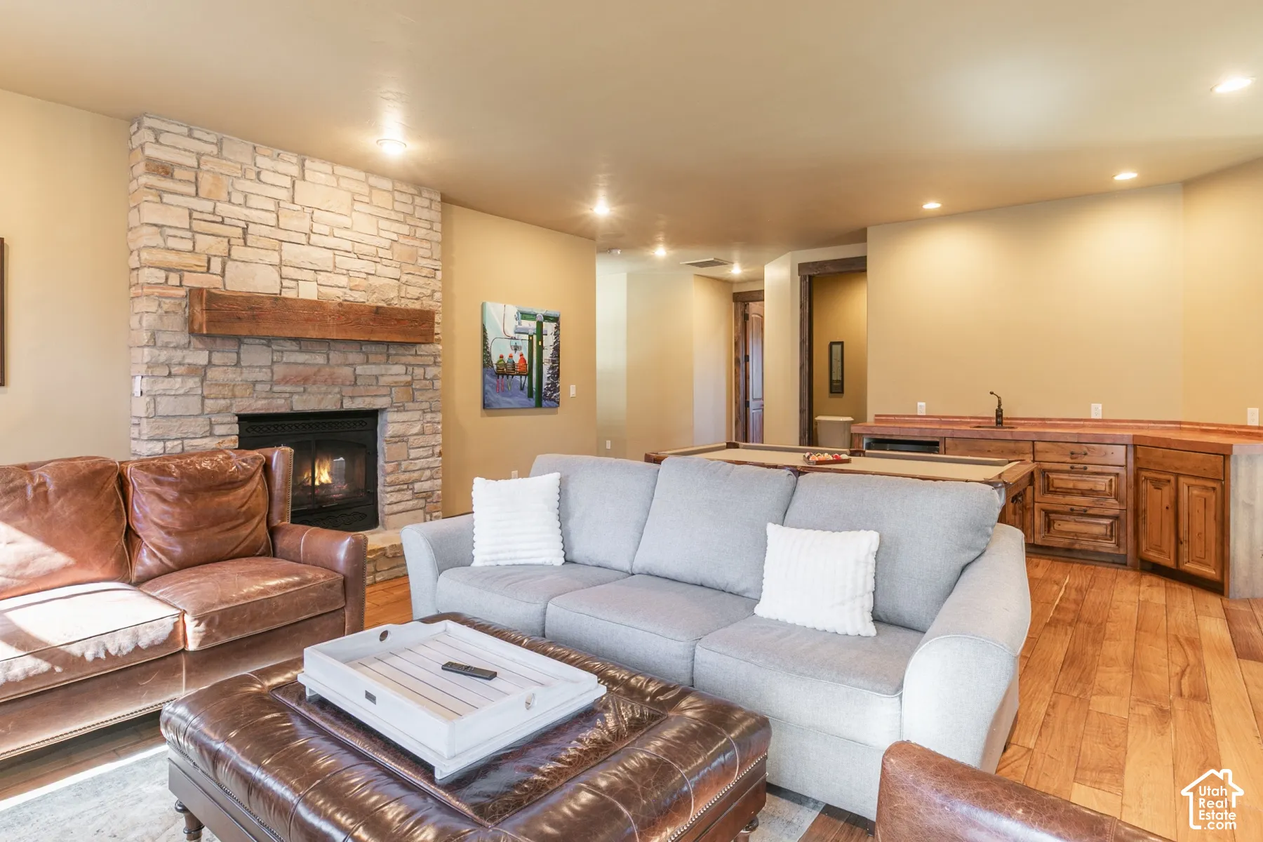 Floor-to-ceiling stone fireplace with a thick timber mantel, wood-finish flooring, and built-in wet bar featuring custom wood cabinetry and a dedicated sink