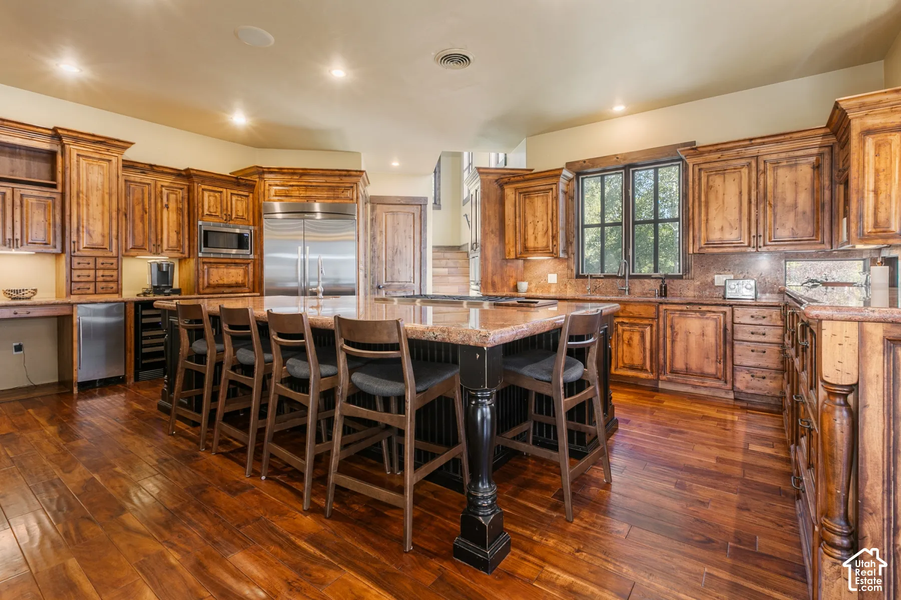 Kitchen featuring custom knotty wood cabinetry, stone countertops, a large central island with seating, built-in stainless steel appliances, and wood flooring