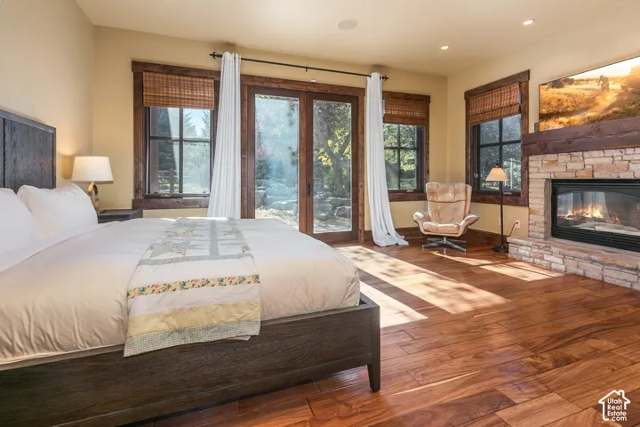 Wood-finish flooring, stone-faced fireplace with a timber mantel, natural wood window trim, and double glass doors