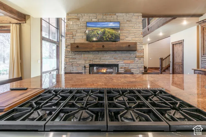 Polished stone countertop featuring an integrated gas cooktop with heavy-duty cast iron grates, paired with a floor-to-ceiling stone fireplace featuring a substantial timber mantel and exposed wooden ceiling beams