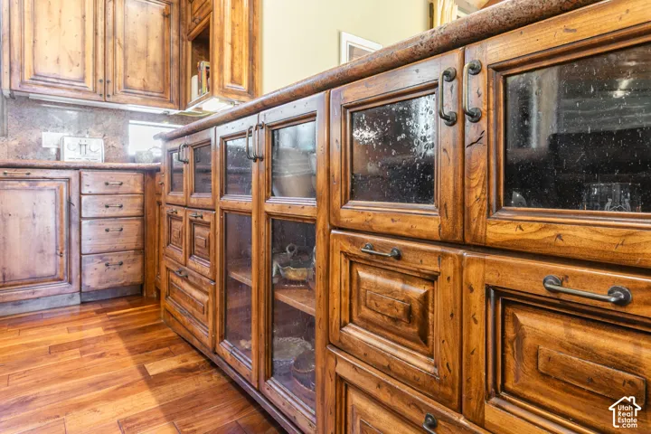 Custom stained-wood cabinetry featuring glass-paneled display doors, stone countertops, and dark metal hardware throughout
