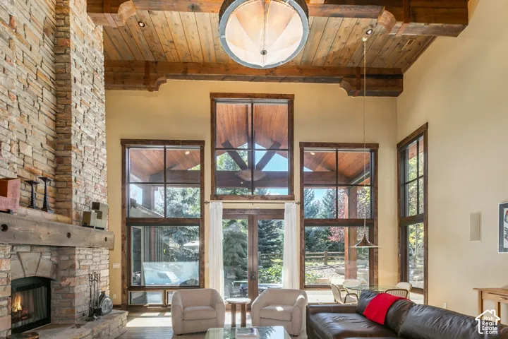 Floor-to-ceiling stone fireplace with a thick timber mantel, vaulted ceilings with exposed structural wood beams, and expansive multi-pane windows featuring wood trim