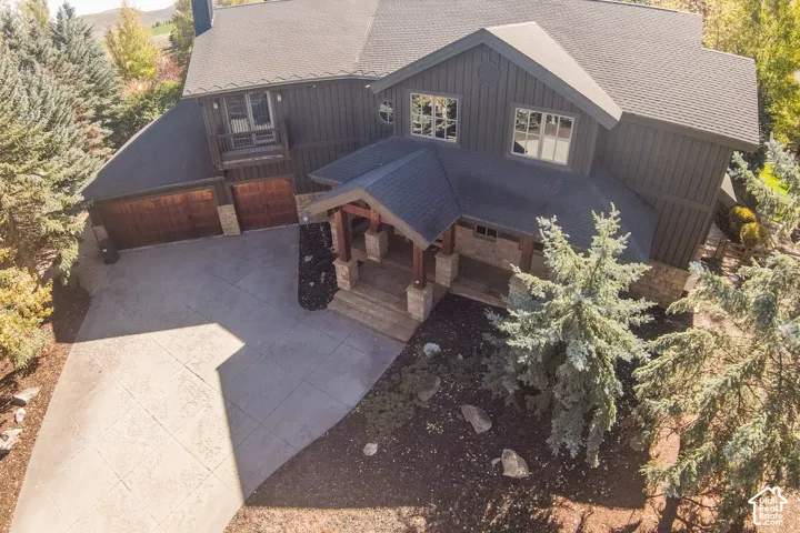Multi-level exterior featuring dark vertical siding, stone masonry accents, a covered front entryway with timber posts, and a paved concrete driveway