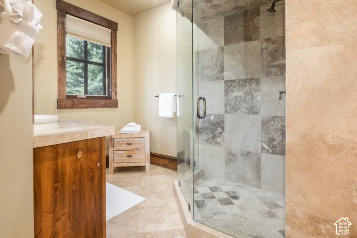Bathroom featuring a corner glass-enclosed shower with tiled walls, stone-finish flooring, custom wood-finish cabinetry, and a window framed by natural wood trim