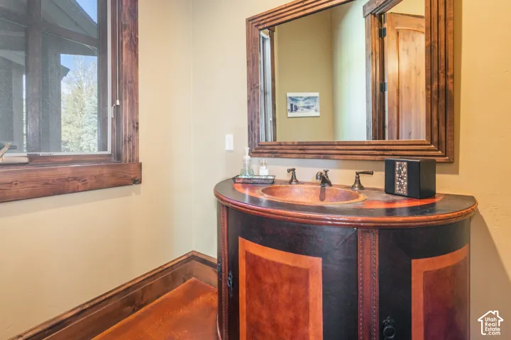 Custom-built rounded vanity with dark wood finish and inset copper basin, dark wood-framed wall mirror, and natural wood window trim