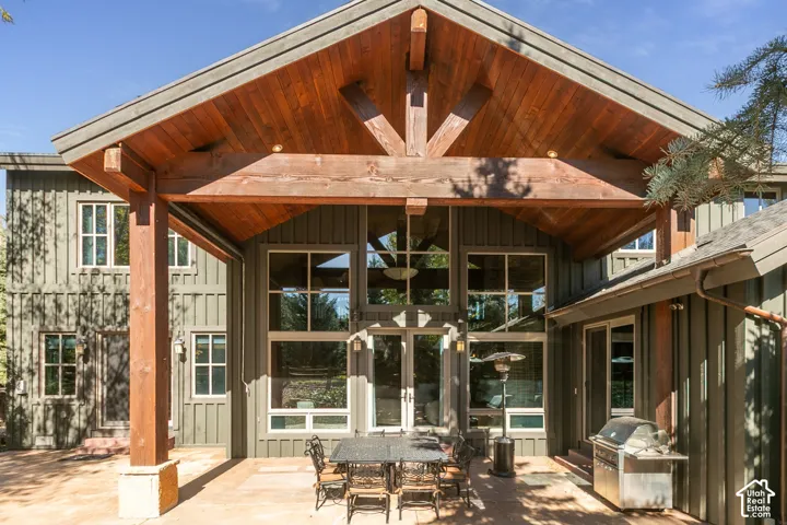 Covered patio featuring a timber-frame gable roof, vertical siding, floor-to-ceiling multi-pane windows, and a paved stone floor