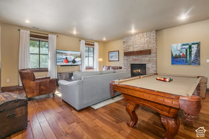 Stone fireplace featuring a rustic timber mantel, wood-finish flooring, and recessed ceiling lighting