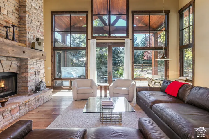 Floor-to-ceiling multi-pane windows, vaulted wood-plank ceiling, natural stone fireplace with timber mantel, and wood-finish flooring