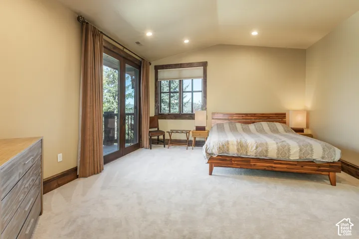 Vaulted ceilings featuring recessed lighting, carpeted flooring, and dark wood-trimmed window casings, including a glass-paned door opening to an exterior deck