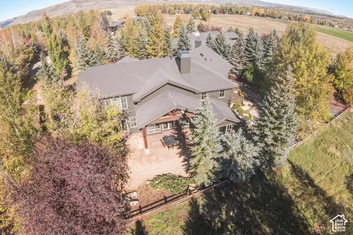 Aerial view of a multi-level residence with dark vertical siding, a metal roof, prominent chimney stack, stone-surfaced patio, and timber-frame gable accents