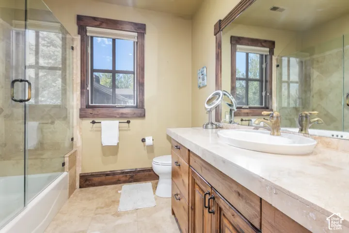 Bathroom featuring a custom wood vanity with stone countertop, vessel sink, walk-in shower with glass enclosure, and natural stone tile flooring