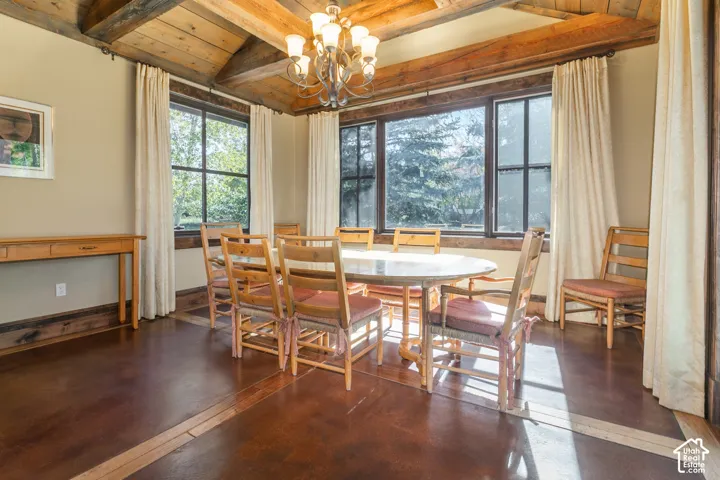 Vaulted ceiling featuring exposed timber beams, stained concrete flooring with wood inlay borders, multi-pane windows, and a classic metal chandelier