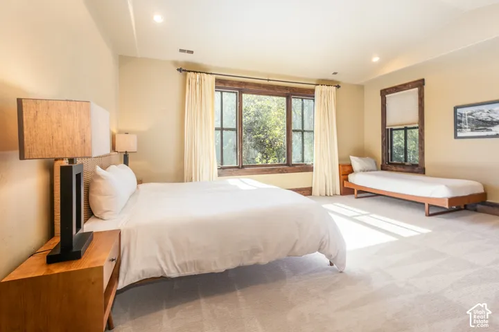Spacious room featuring vaulted ceilings, neutral wall-to-wall carpeting, and multi-pane windows framed in natural wood