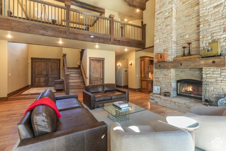 Great room featuring vaulted ceilings, a floor-to-ceiling stone fireplace with a timber mantel, wood-finish flooring, a mezzanine balcony with wood railing, and custom millwork