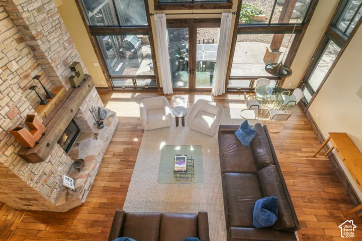 Double-height living area featuring floor-to-ceiling windows, natural stone fireplace, heavy timber mantel, and wood-finish flooring