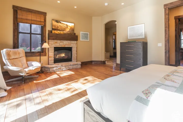 Fireplace featuring a stone surround and timber mantel, wood-finish flooring, recessed lighting, and arched doorway