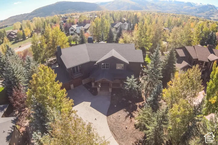 Aerial perspective of a multi-level residence featuring dark wood-finish exterior siding, stone-accented columns, a paved driveway, and mountain scenery