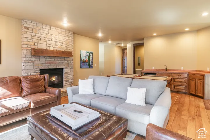 Floor-to-ceiling stone fireplace with a thick timber mantel, wood-finish flooring, and built-in wet bar featuring custom wood cabinetry and a dedicated sink