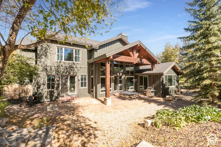 Board-and-batten exterior siding, expansive stone patio, covered timber-frame porch, multi-pane floor-to-ceiling windows, and mature evergreen trees