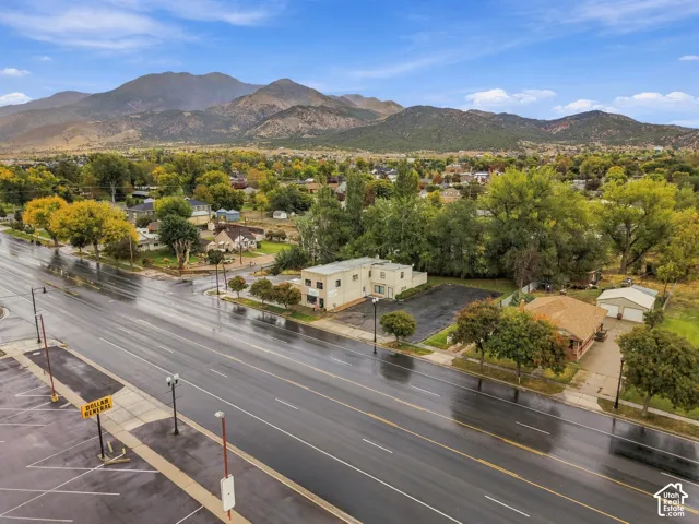 Aerial perspective featuring a multi-story commercial structure with an asphalt parking lot, mature trees, and a mountain range backdrop